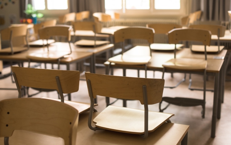 Uppställda stolar på skolbänkar i ett tomt klassrum.